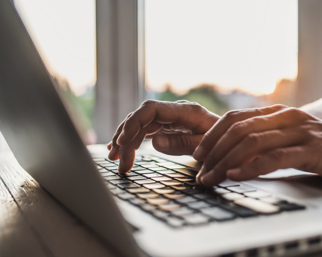 Hands typing on a laptop keyboard near a sunny window.