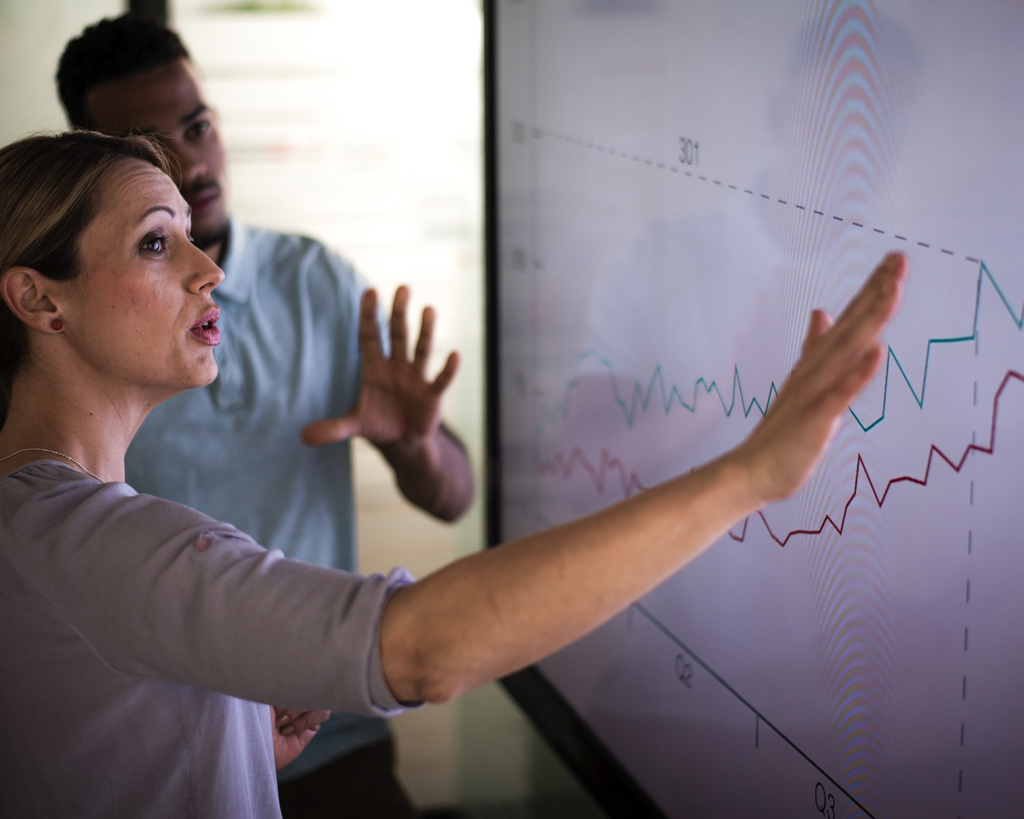 Businesswoman and colleague analyzing data on a large screen.