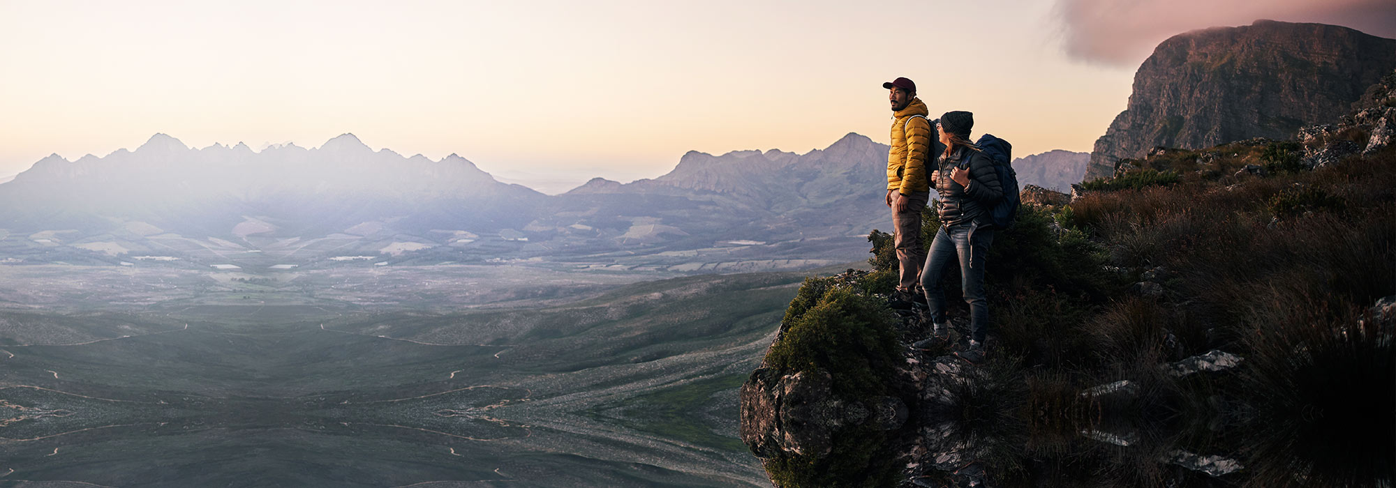 Hikers standing on a mountain edge at sunrise with a panoramic view.