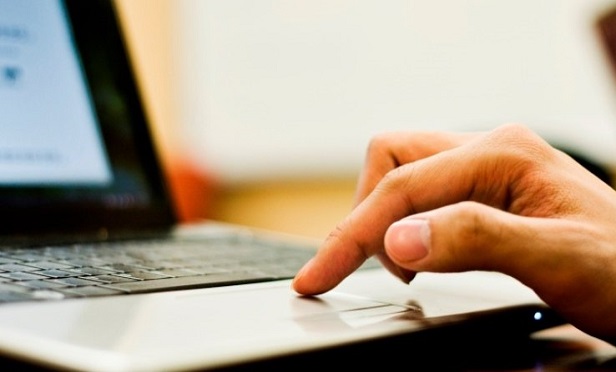 Hand typing on laptop touchpad for computer navigation.