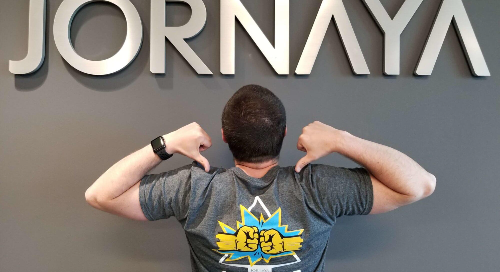 Person pointing at a graphic on their t-shirt while standing in front of a Jornaya sign.