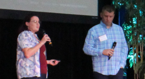 Two people on stage holding microphones during a presentation.