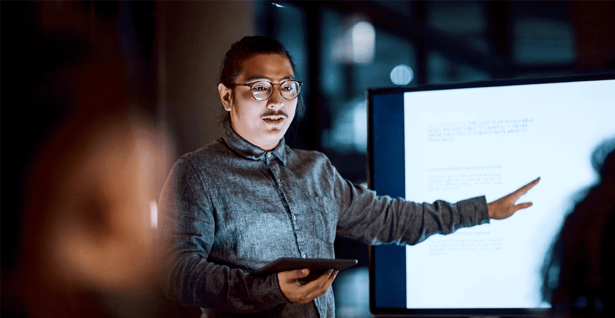 Young professional giving a dynamic presentation with a tablet and screen.