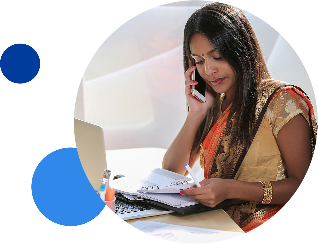 Woman in traditional attire working at a desk while talking on the phone.