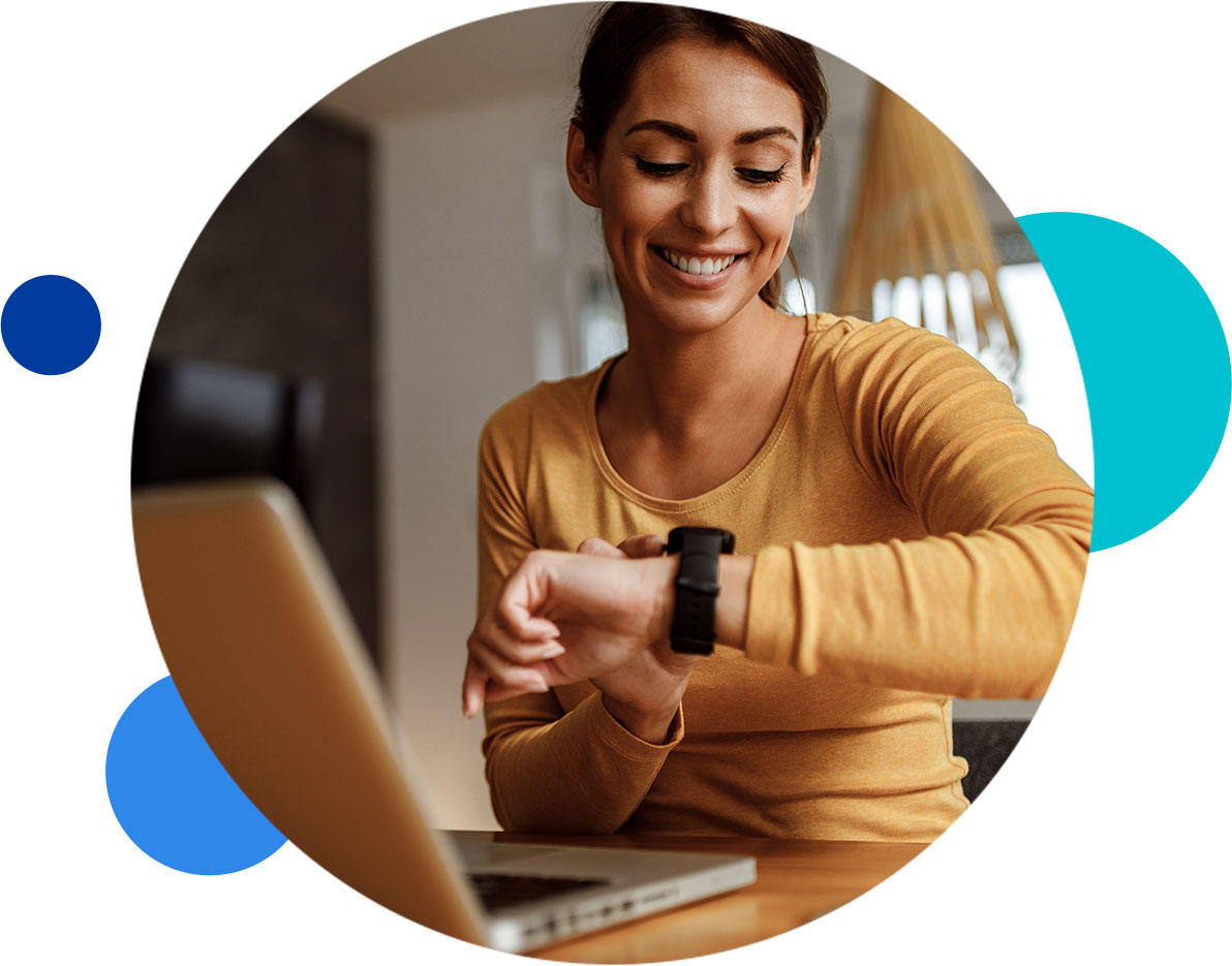 Woman smiling while checking her smartwatch at a desk with a laptop.