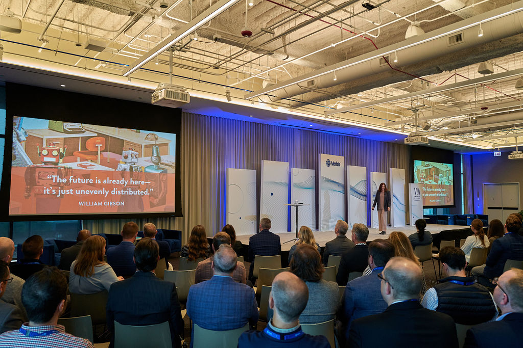 L1081359 Audience watching a presentation on future technology trends in a modern conference room.