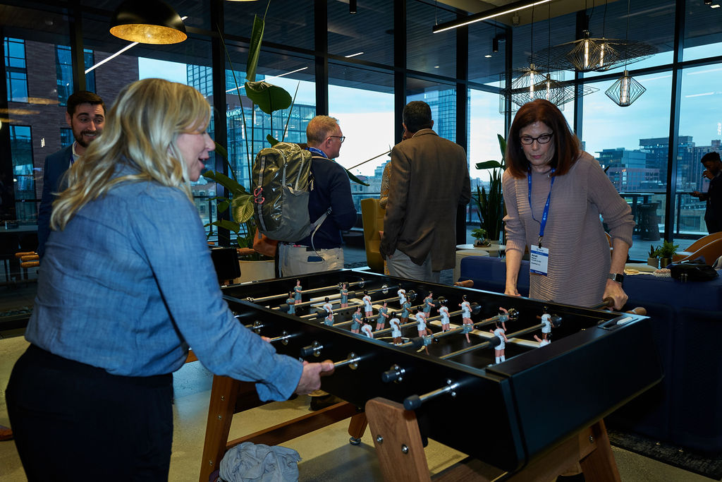 L1081577 Colleagues playing foosball at a modern office event with city view.