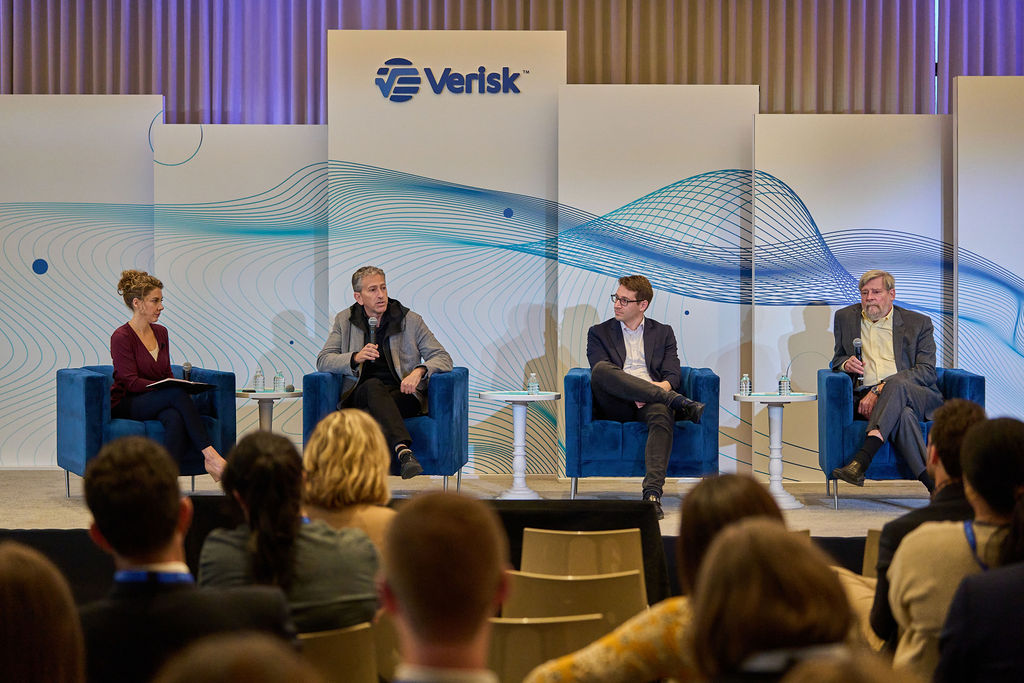 _P1_3919 Panel discussion at a Verisk conference with four speakers and an audience.