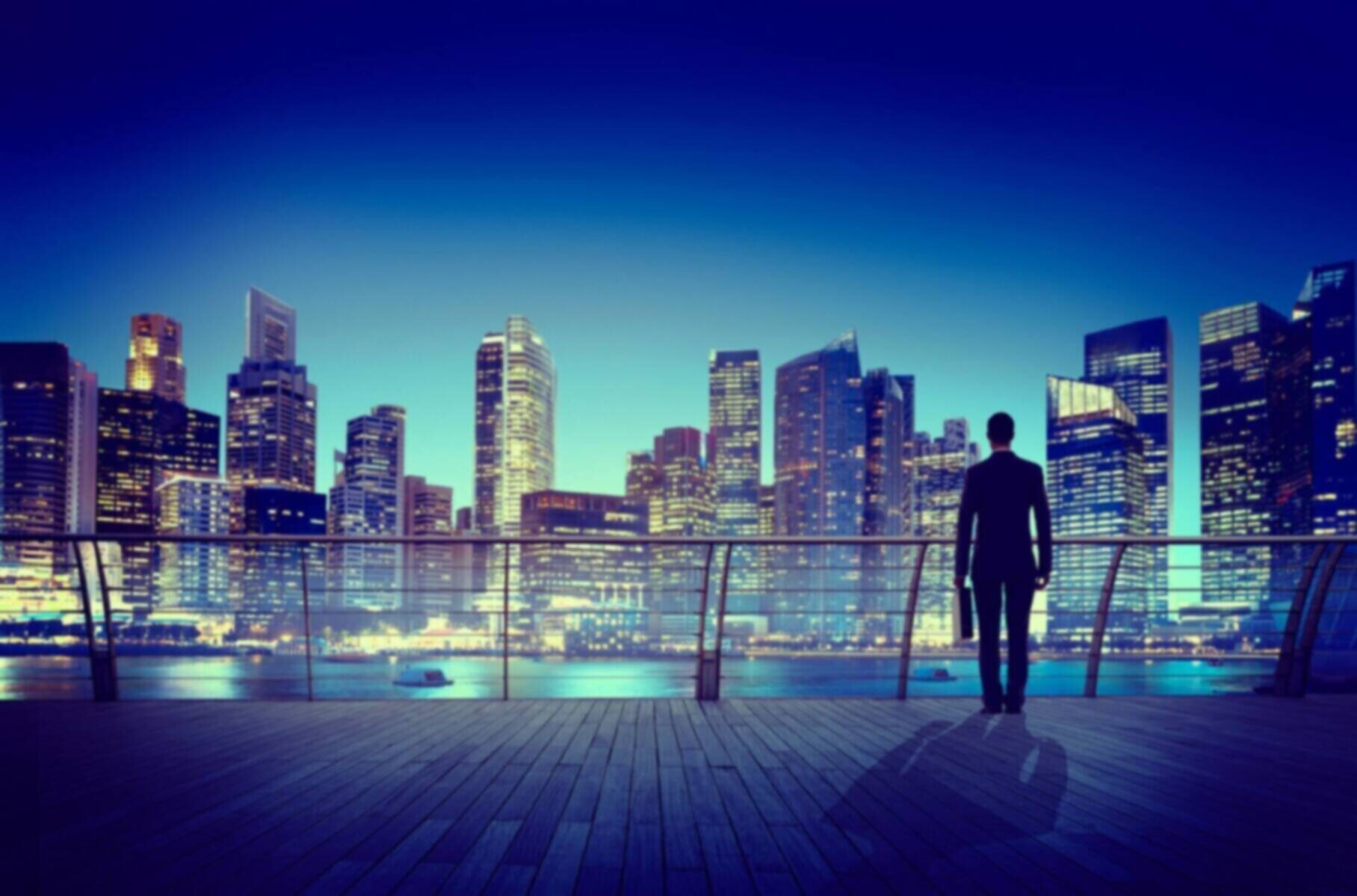 Silhouette of a businessman overlooking a modern cityscape at dusk.