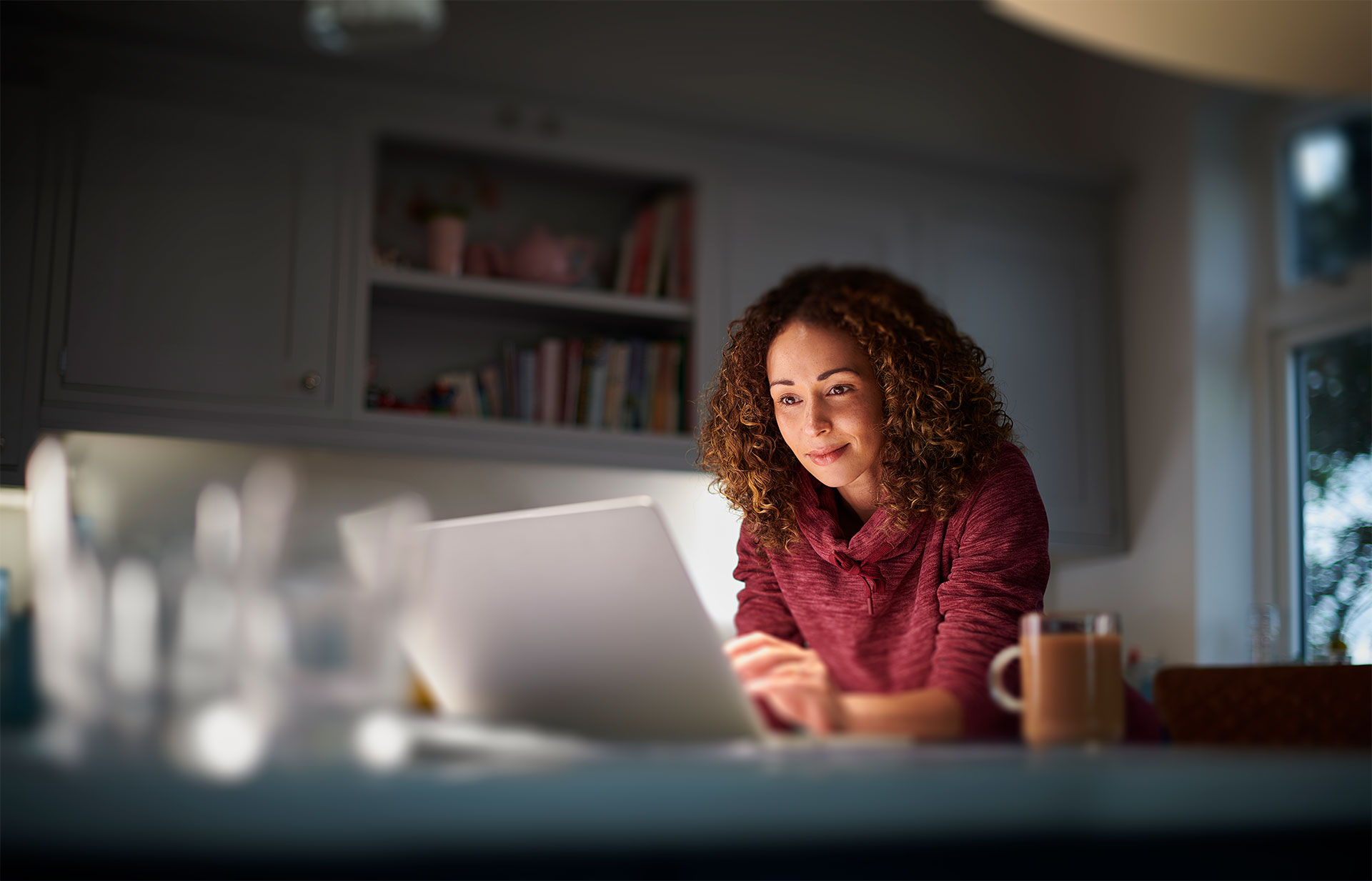 A person with curly hair working on a laptop in a cozy kitchen setting.