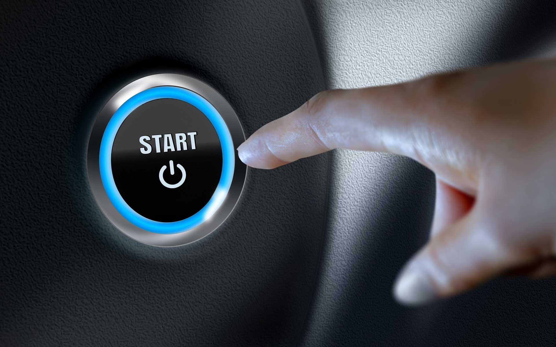 a person's hand just about to push the start button of a vehicle, representing their intent to move forward with a purchase