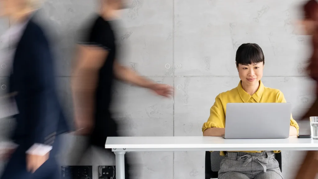 Busy Office Featuring a Focused Professional smiling on a laptop at her desk